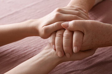 Young and elderly women holding hands together on pink fabric, closeup