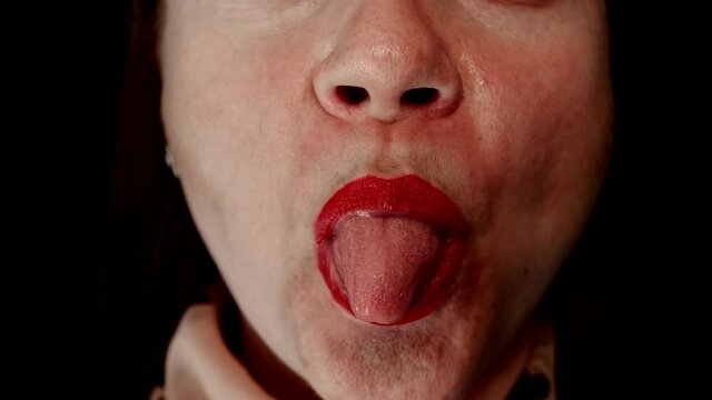 Close-up of a woman's mouth with bright red lipstick. She shows her teeth, smiles, tongue and licks her lips.