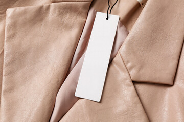 Blank white tag on beige leather jacket, top view. Space for text
