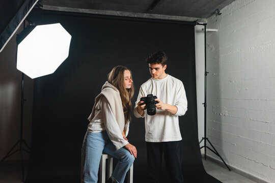 Photographer showing pictures on photo camera to female in studio