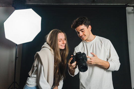 Photographer showing pictures on photo camera to female in studio