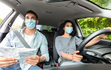 Husband and wife in face masks driving auto