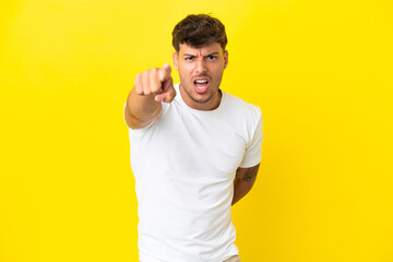 Young caucasian handsome man isolated on yellow background frustrated and pointing to the front