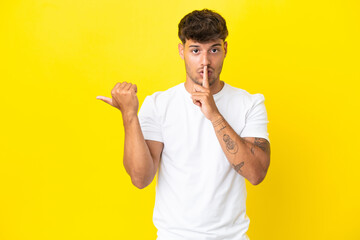 Young caucasian handsome man isolated on yellow background pointing to the side and doing silence gesture