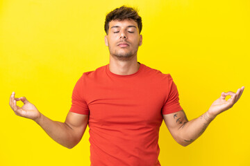 Young caucasian handsome man isolated on yellow background in zen pose