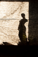 silhouette statue of a woman behind a paper wall with sun. Greek statue with only one hand