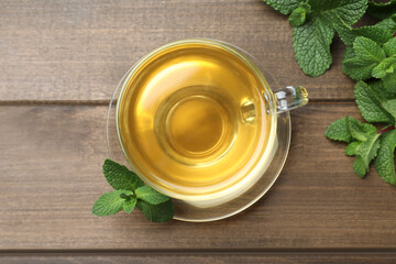 Cup of aromatic green tea with fresh mint on wooden table, flat lay