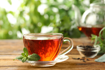 Glass cup of aromatic black tea with fresh mint on wooden table against blurred background. Space for text