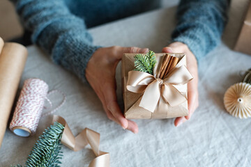 A girl holds a Christmas gift decorated with ribbons and natural decor.