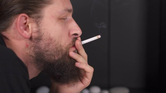man smoke cigarette. Caucasian guy with beard look aside from side and blows smoke. Smoking is bad for your health. Light cigarette and light cigarette with a lighter. fire burns near person face.