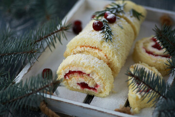 Homemade cakes and desserts. Sponge roll with cottage cheese filling, berry jam on a white wooden board with fir branches and red berries. Winter atmosphere, rustic