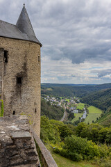 Fototapeta na wymiar Castle tower, countryside landscape with hills covered with lush green trees, town of de Bourscheid, country road and its river in the background, cloudy day with a sky with gray clouds, Luxembourg