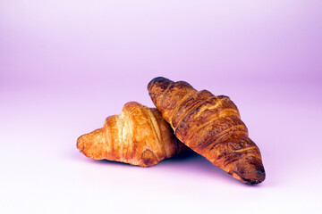 Two fresh croissants on pastel pink background.