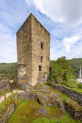 Fototapeta na wymiar Square tower with windows on a rocky surface of the ruined castle of Esch-sur-Sure surrounded by hills with lush green trees, sunny summer day with a blue sky and white clouds in Luxembourg
