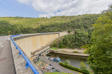 Fototapeta premium Top view of the huge wall, hydroelectric complex, parking lot of the Esch-sur-Sure dam, hills with lush green trees and wild vegetation in the background, cloudy day in Luxembourg