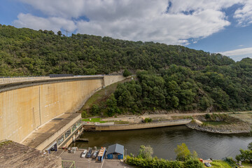 Obraz premium Top view of the Esch-sur-Sure dam, huge wall, hydroelectric complex, parking lot, hills with lush green trees and wild vegetation in the background, cloudy day with abundant clouds in Luxembourg