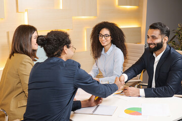 Great work. Strong handshake of intelligent male businesspeople. Elegant men are sitting in office wearing formal clothes with their female colleagues