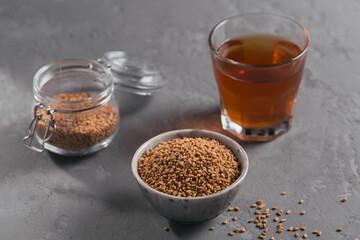Glass of Egyptian fenugreek yellow tea, Helba or Methi Dana drink and fenugreek seeds on grey background