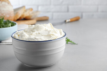 Bowl of tasty cream cheese on grey table. Space for text