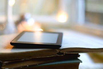 Stack of books, digital e-reader and lit candles. Selective focus.