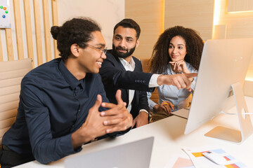Team of young and successful employees listen to progress report from male employee at the morning meeting. Multiracial guy pointing at the computer screen in the office