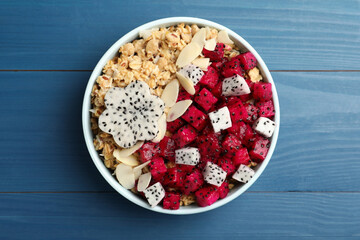 Bowl of granola with pitahaya and almond petals on blue wooden table, top view