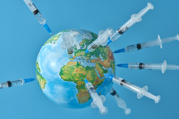 A globe studded with a lot of syringes with a vaccine on a light blue background close-up. Concept....