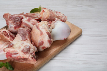Cutting board with raw chopped meaty bones and basil on white wooden table, closeup. Space for text