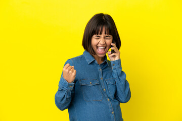 Pregnant woman using mobile phone isolated on yellow background celebrating a victory