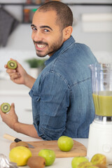 young happy man in kitchen tasting kiwi fruits
