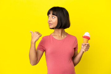 Pregnant woman holding a cornet ice cream isolated on yellow background pointing to the side to present a product