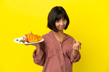 Pregnant woman holding waffles isolated on yellow background making money gesture