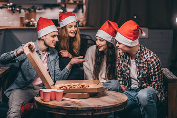 Young people in Santa's hats celebrate Christmas. A man with a disability with friends at new Year...