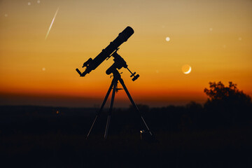 Silhouette of telescope and countryside under the starry skies.