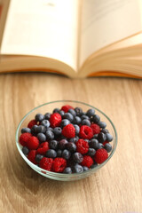 Bowl of blueberries and raspberries and open book on a table. Selective focus.