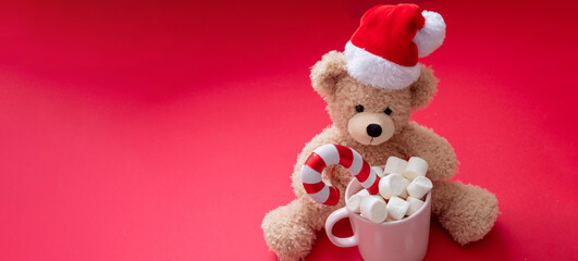 Santa teddy and Christmas hot beverage, mug with marshmallows and candy cane on red color background