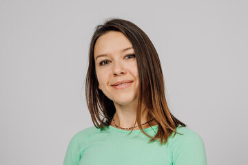 Fototapeta premium Portrait of smiling young woman. Beautiful happy brunette is smiling and posing on gray isolated background, she is wearing green jacket.