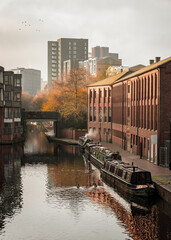 Birmingham gas basin narrowboat with moored canal boats and cityscape modern skyline behind. Sunny beautiful view waterways with bridge, barges and downtown tower block sky scrapers. Birds in sky. - obrazy, fototapety, plakaty