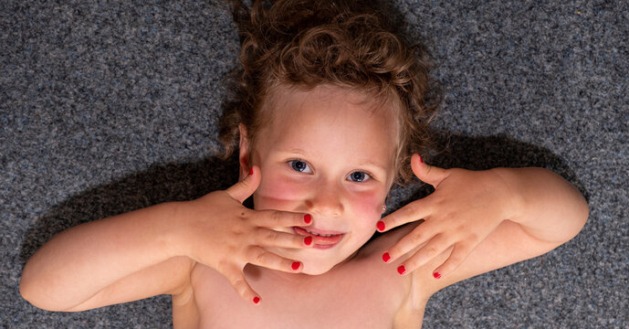Child, girl 5 years old painted her nails on her hands with red varnish. Devosca is happy and shows her hands.