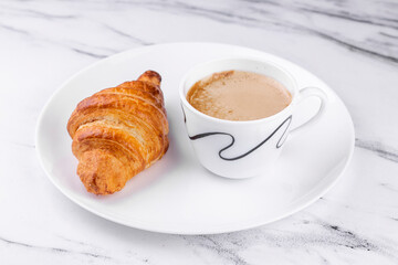 White ceramic plate with Cup of coffee and croissant on marble texture background.