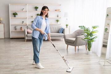 Portrait of cheerful woman cleaning floor with spray mop