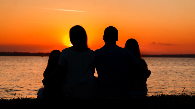 The family watches the sunset. Bright sun. Silhouette of a family by the river. Happy family together.