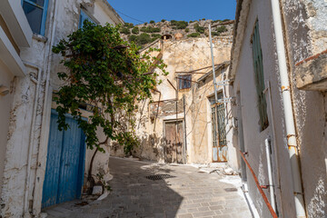 Fototapeta na wymiar Eine kleine verwinkelte Gasse in einem Bergdorf auf Kreta, Griechenland mit altertümlichen Häusern und einer blauen Tür (Querformat)