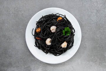 Flat lay black pasta with seafood isolated on white plate on gray background. Top view.