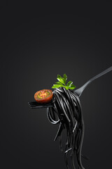 Black pasta rolled on a fork isolated on black background   with copyspace. Vertical format....