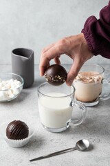 Woman's hand dropping chocolate cocoa bomb into hot cup of milk. Holiday winter drink. Handmade...