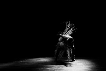 Contemporary dancer dancing in theater with black background and straw accessory.