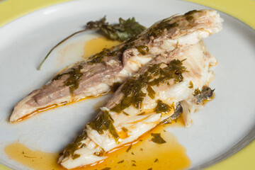 Plating of baked sea bream with a dressing of garlic sauce, vinegar, oil, and a sprig of parsley in a decorated artisan plate ready to serve. Fish and food.