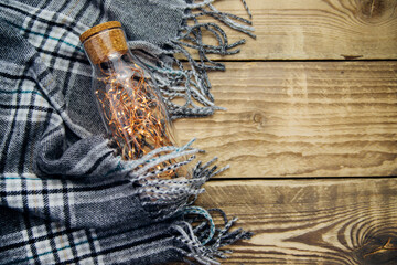 A garland of Christmas lights in a glass bottle.Warm grey scarf or plaid on a wooden background.