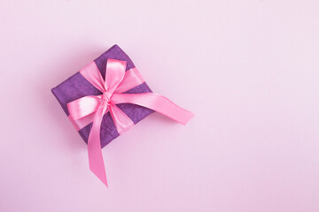 Top view of purple gift box with tied pink bow on the pink background. Copy space.